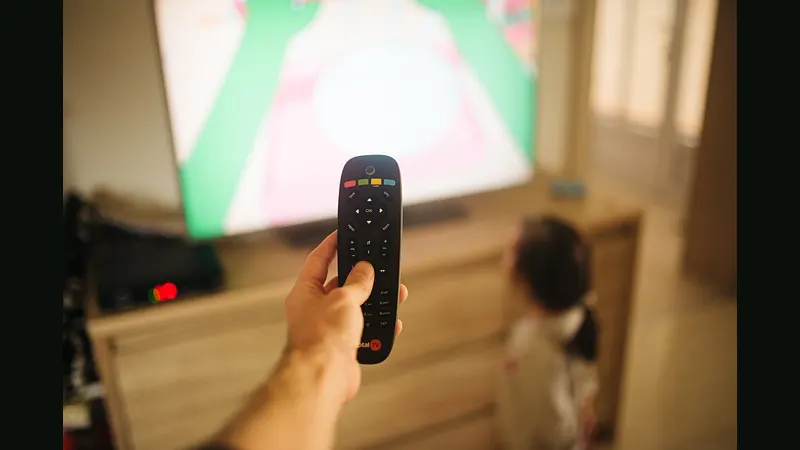 Child watching TV while an adult holds a remote control in a living room